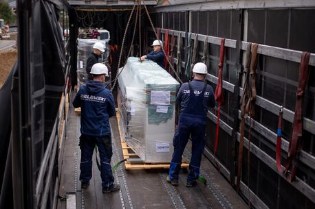 Monteure mit Helmen beim Abladen einer verpackten Kälteanlage mit Kran aus einem LKW-Anhänger