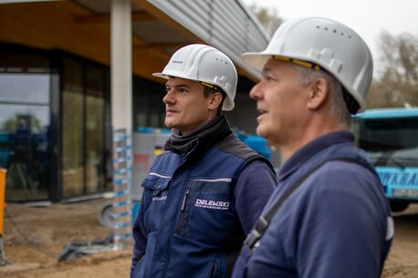 Ein Monteur und ein Projektleiter mit Schutzhelmen betrachten konzentriert eine Baustelle.