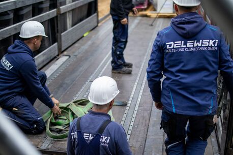 Drei Monteure sichern mit Gurten auf einem LKW Ladung. Die Szene zeigt sorgfältige Vorbereitung für den sicheren Transport.