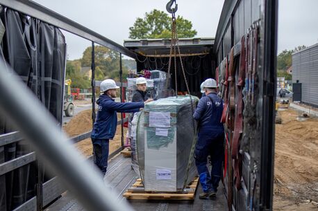 Monteure mit Helmen beim Abladen einer verpackten Kälteanlage mit Kran aus einem LKW-Anhänger