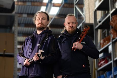 Zwei Mitarbeiter stehen nebeneinander und halten Werkzeuge in den Händen.